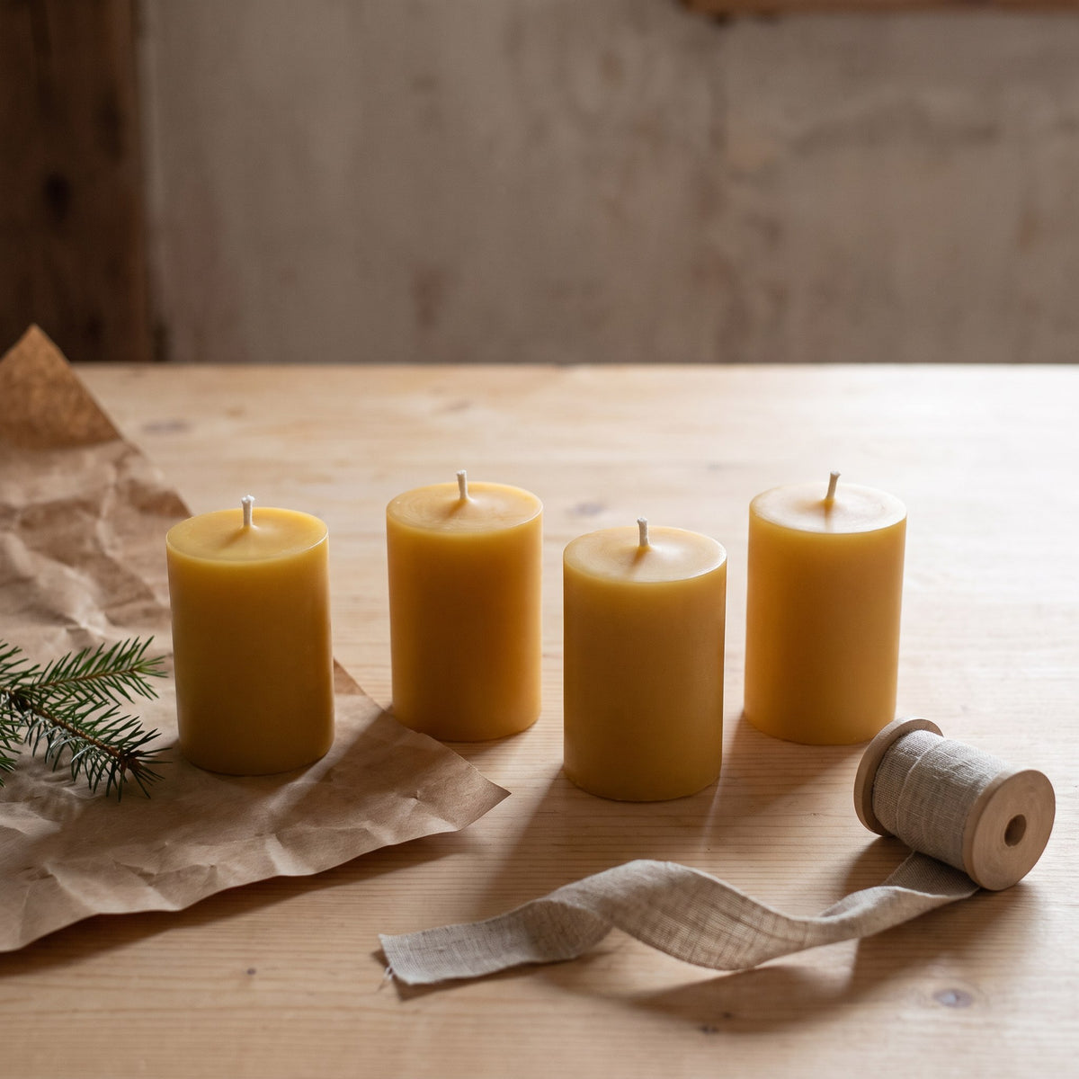 Vier Adventskranz-Kerzen aus Bienenwachs stehen neben Packpapier, Leinenband und Tannenzweig