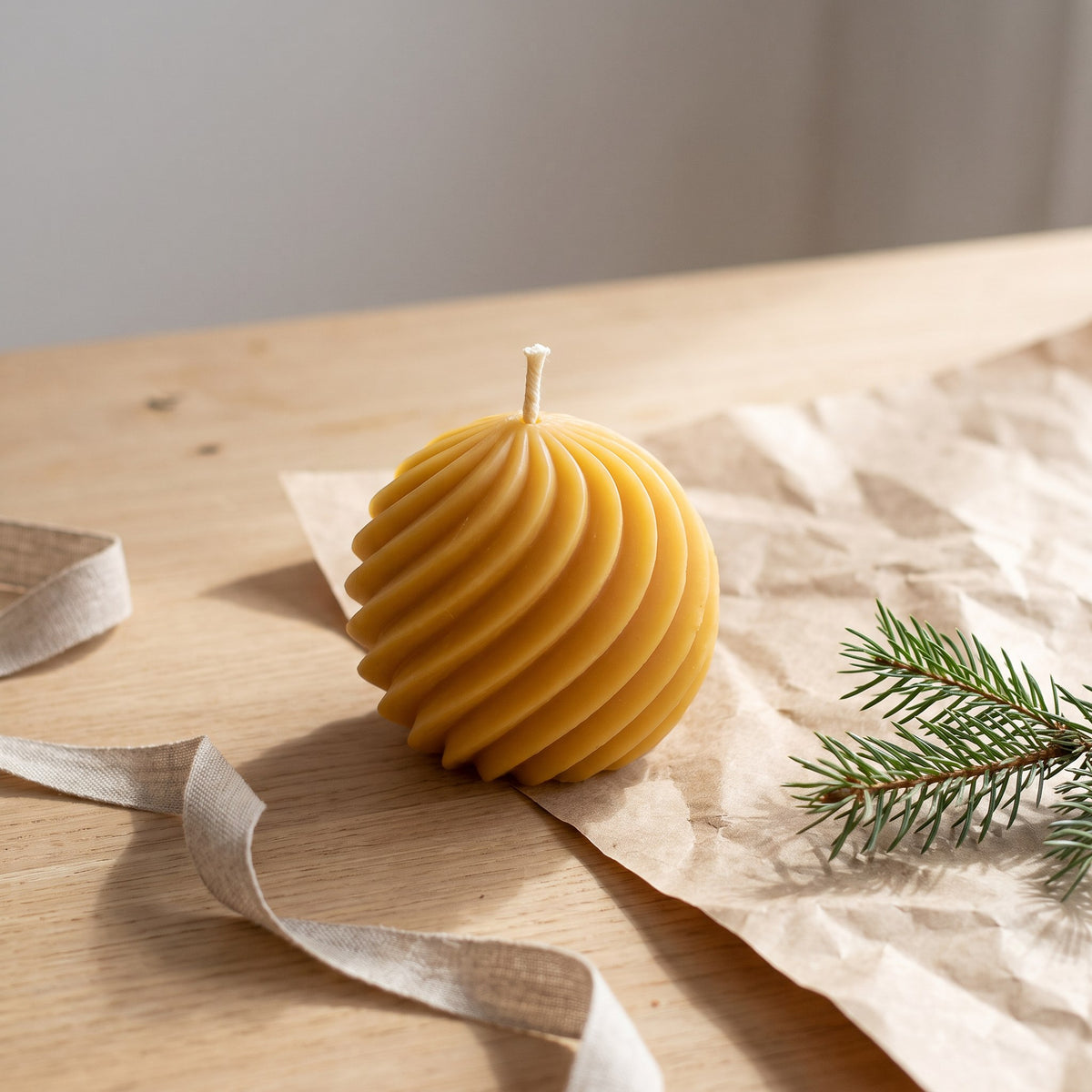Spiralkugel aus Bienenwachs steht neben Packpapier, Leinenband und Tannenzweig