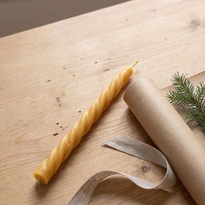 Spiralkerze aus Bienenwachs steht neben Packpapier, Leinenband und Tannenzweig
