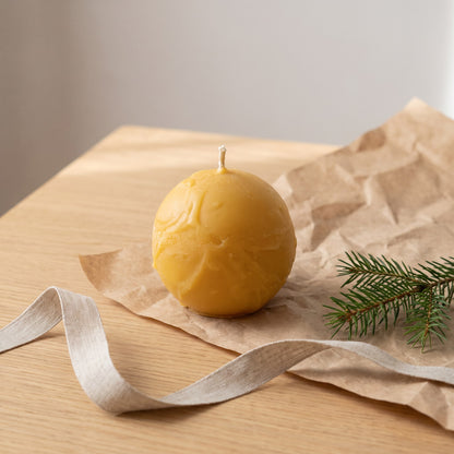 Strukturkugel aus Bienenwachs steht neben Packpapier, Leinenband und Tannenzweig