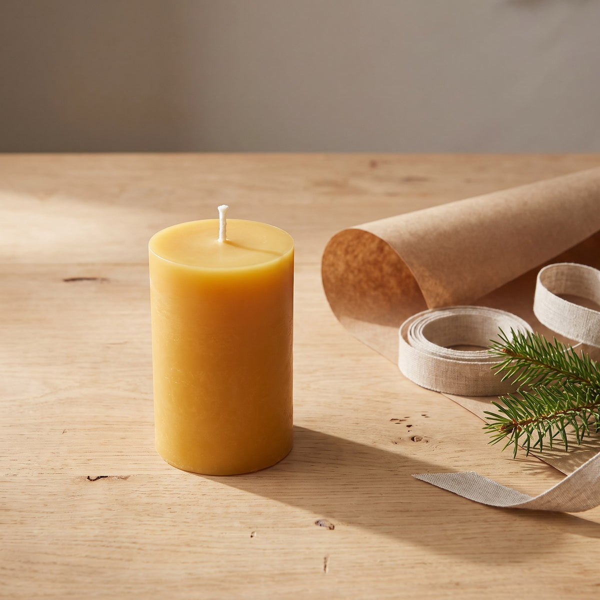 Stumpenkerze aus Bienenwachs steht neben Packpapier, Leinenband und Tannenzweig
