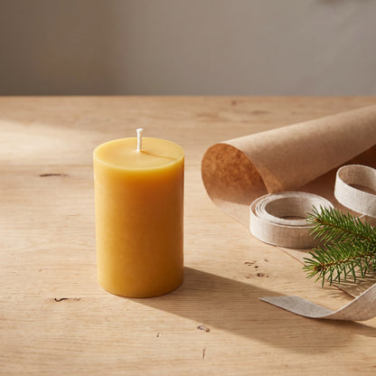 Stumpenkerze aus Bienenwachs steht neben Packpapier, Leinenband und Tannenzweig