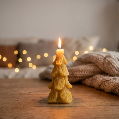 Große Tannenbaum-Kerze aus Bienenwachs brennt abends auf einem Holztisch, im Hintergrund Lichterkette und Strickdecke