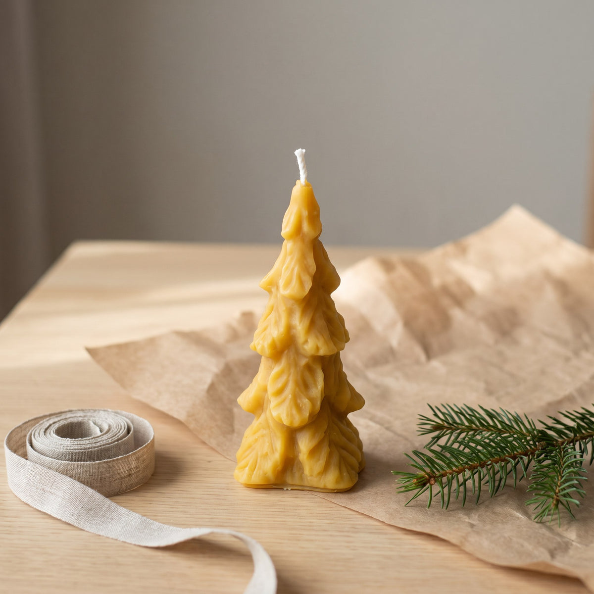 Große Tannenbaum-Kerze aus Bienenwachs steht neben Packpapier, Leinenband und Tannenzweig
