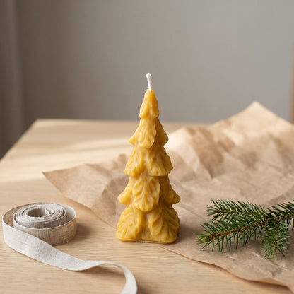 Große Tannenbaum-Kerze aus Bienenwachs steht neben Packpapier, Leinenband und Tannenzweig