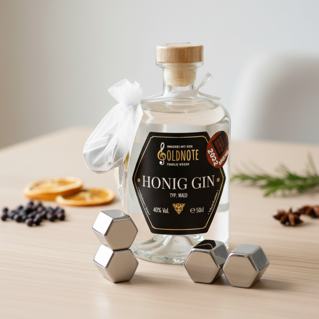 Flasche Goldnote Honig Gin auf Holztisch mit Winter-Botanicals, Orangenscheiben und Metall-Eiswürfeln – elegantes Produktbild des prämierten Honig Gins.